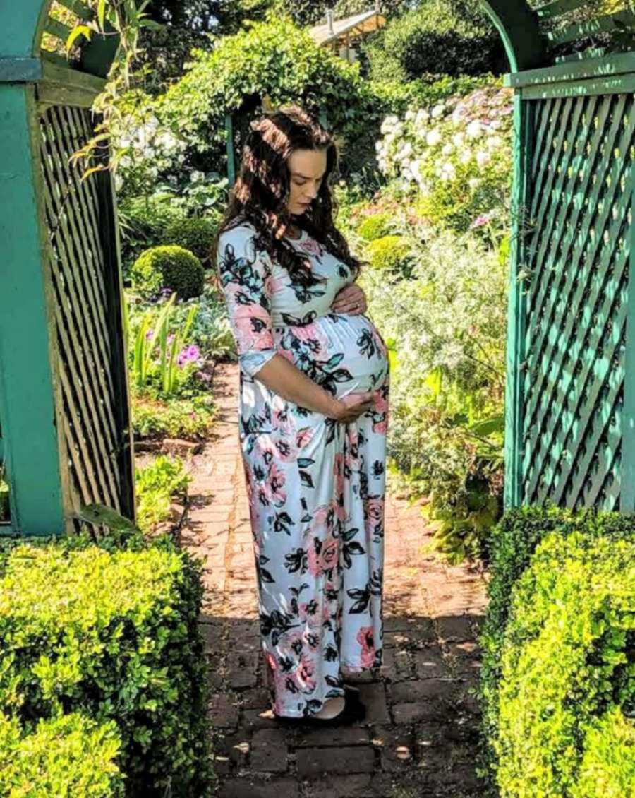 Mom in floral dress holding pregnant belly in garden