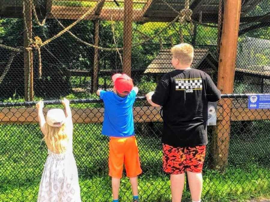 Three siblings leaning against wire fence