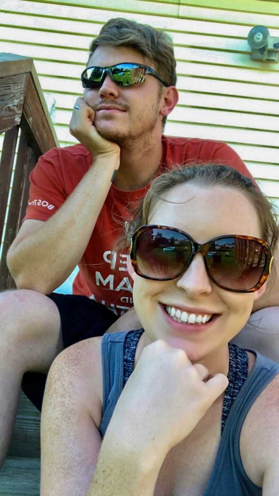 Wife sits on stair below husband and takes a selfie while both are smiling