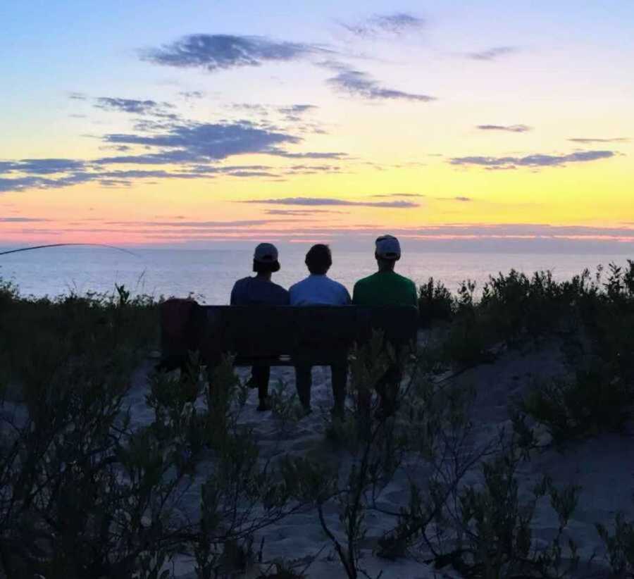 daughter sitting on a bench with her parents, watching the sunset by the water