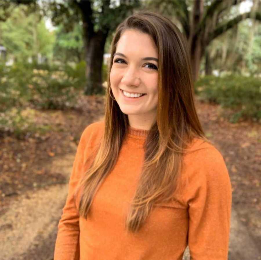 Mom with brown hair and orange shirt smiling in forest