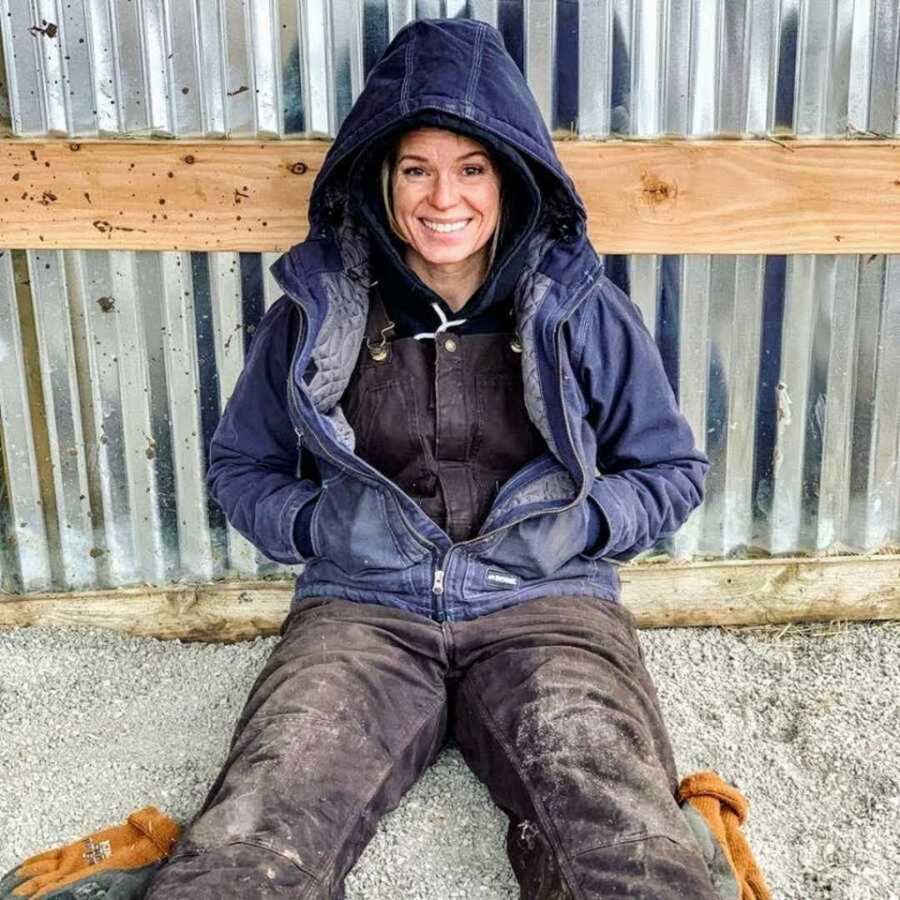 woman smiles while sitting on ground in blue coat