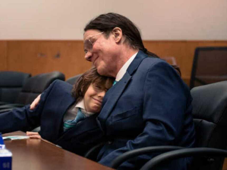 Adoptive father and son smiling and hugging in courtroom