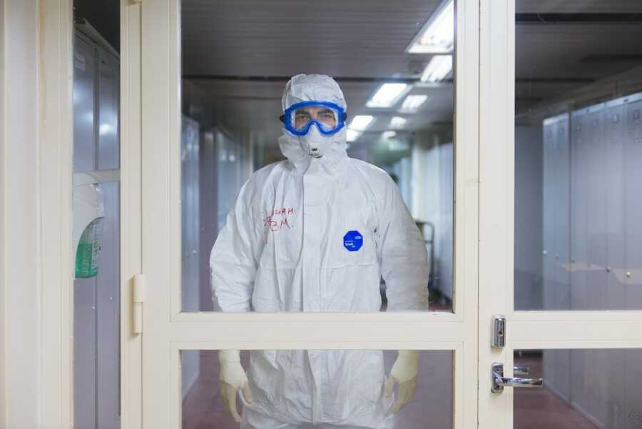 health care worker wearing protective gear head-to-toe standing behind glass door