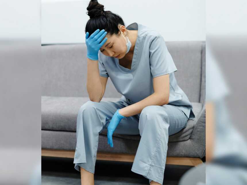 nurse sits tired with head in hand