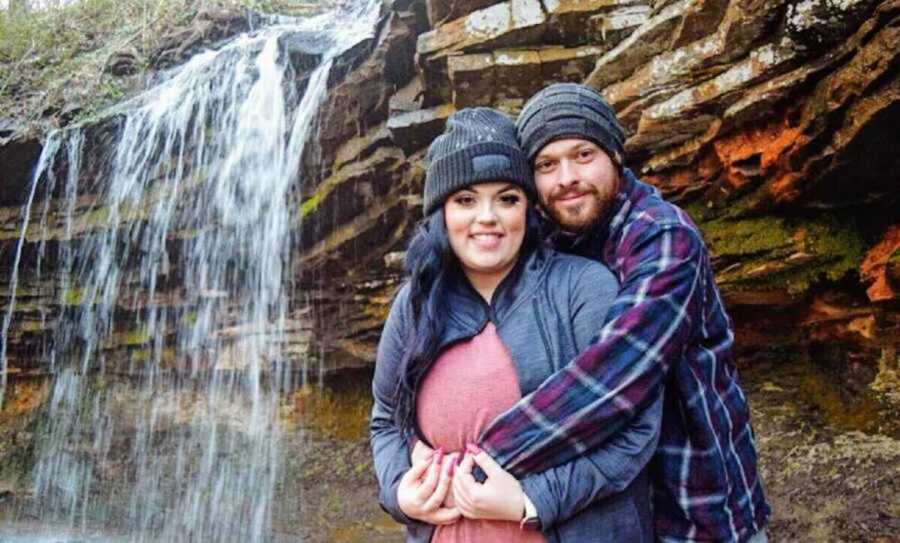 Boyfriend hugs his girlfriend from behind while they are at a waterfall