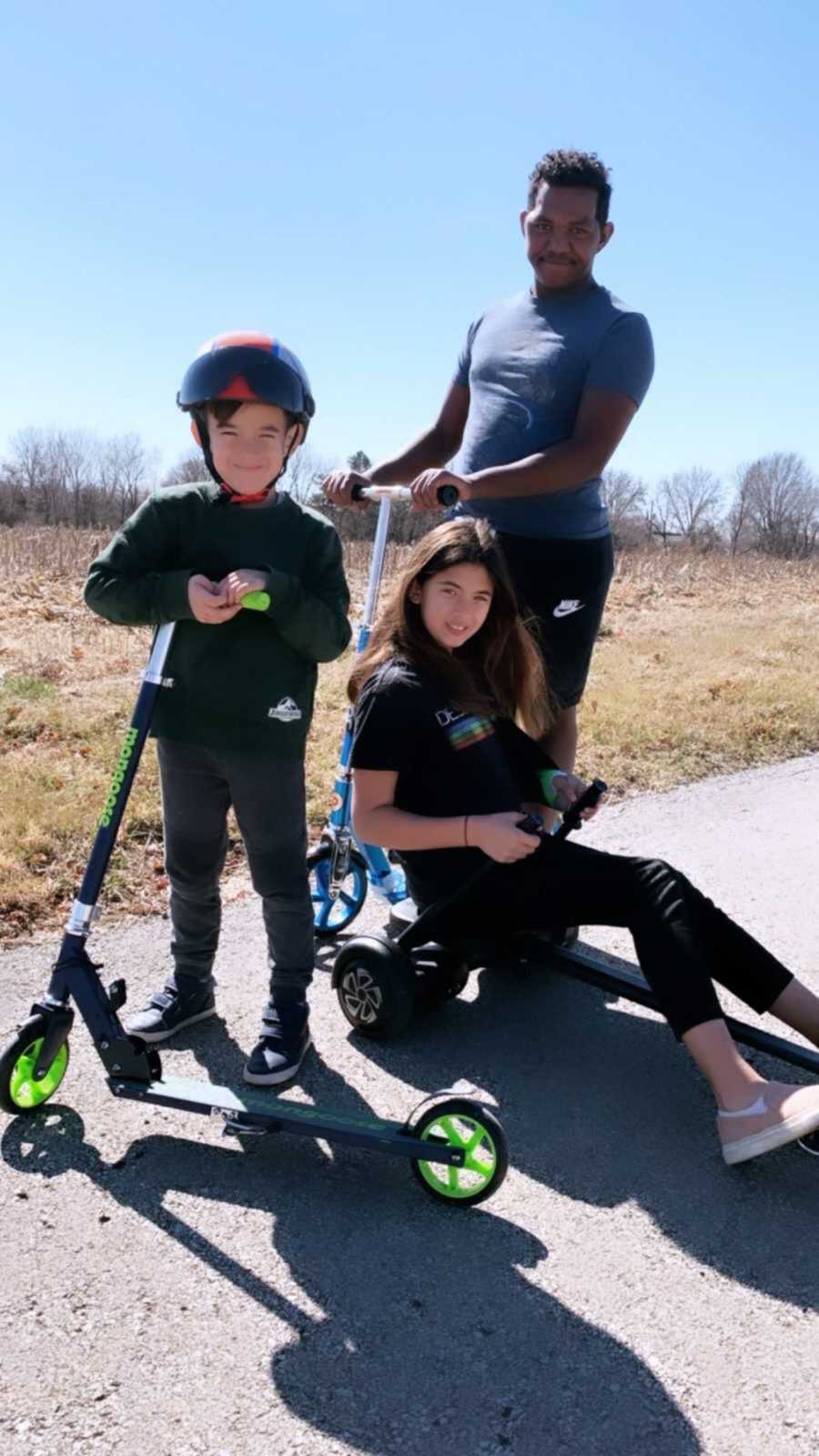 Adopted Brother And Siblings Smiling Outside On Scooters