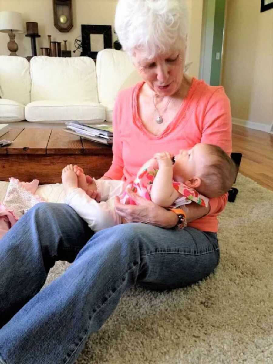 Grandma wearing pink shirt holding infant baby in lap