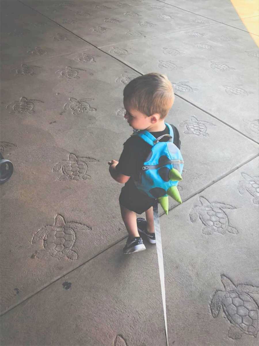Little boy wearing leashed dinosaur backpack