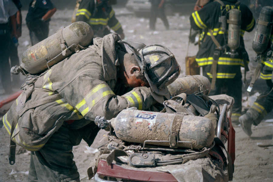 Firemen covered in ash lies over on rubble