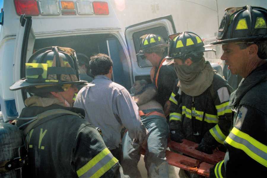 Firefighters help an injured man into the back of an ambulance