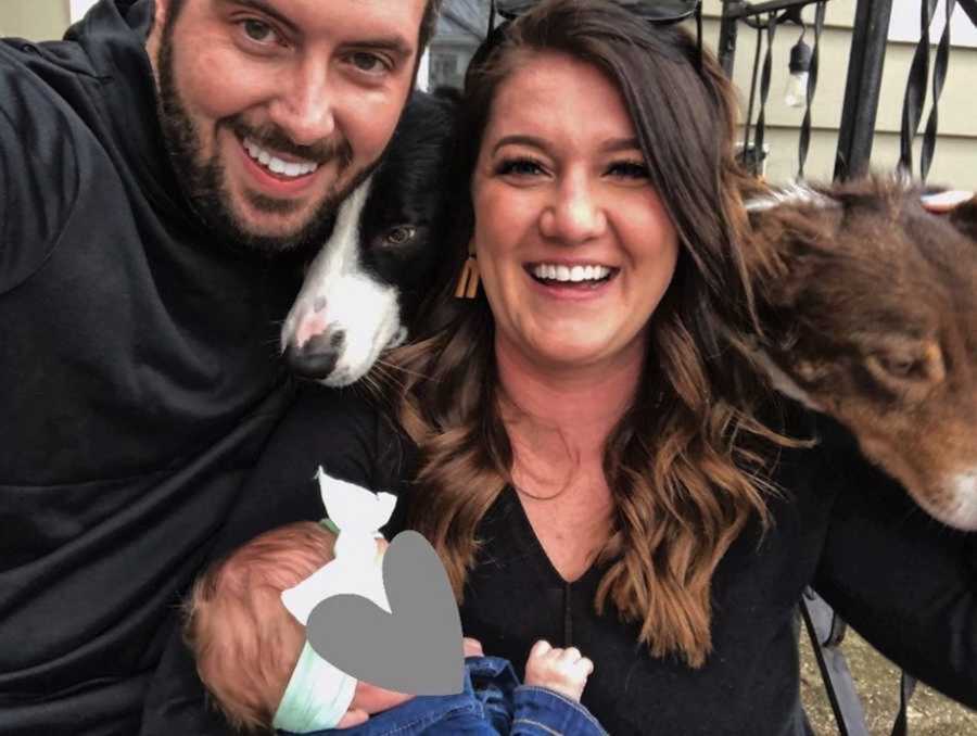 Foster parents smiling next to newborn girl and two dogs