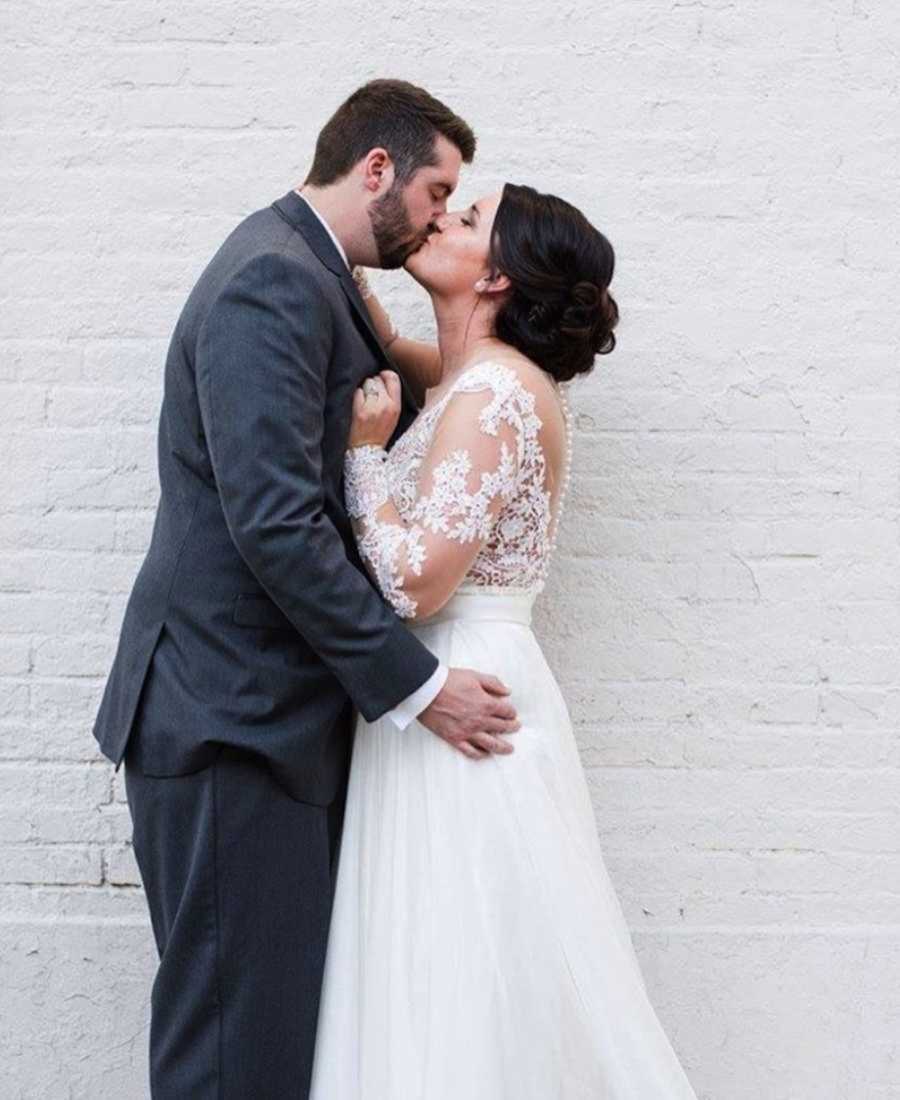 Bride and groom kissing in front of white brick wall