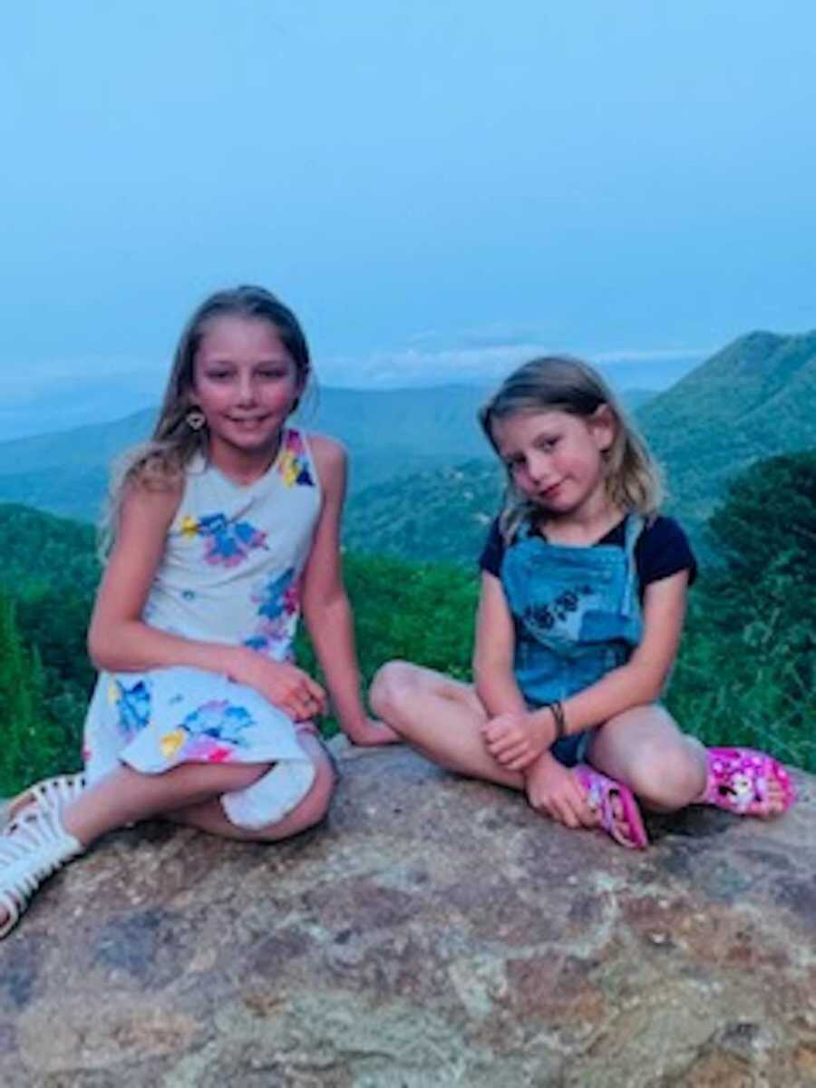 Sisters sitting on rock in front of grassy mountains