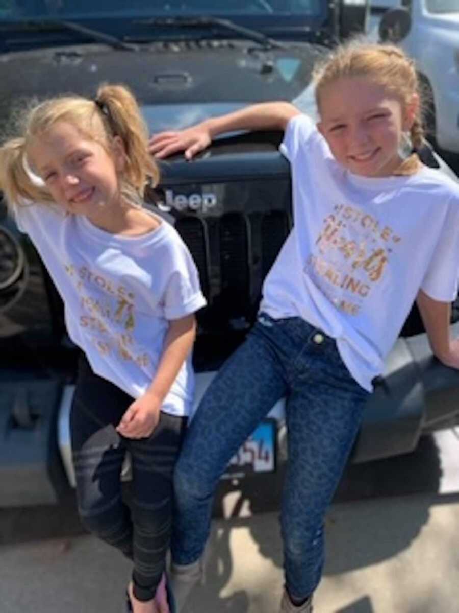 Blonde sisters leaning against Jeep in matching white shirts