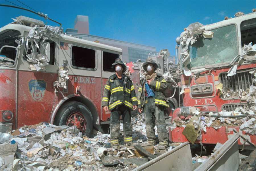 Two first responders standing in debris and alongside two firetrucks