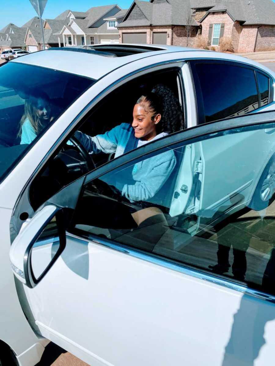 Teen foster child driving silver car next to sister in passenger seat