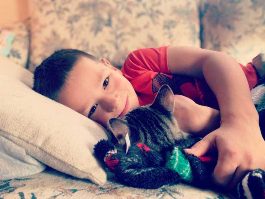 Little boy lying down as he embraces the white and brown cat