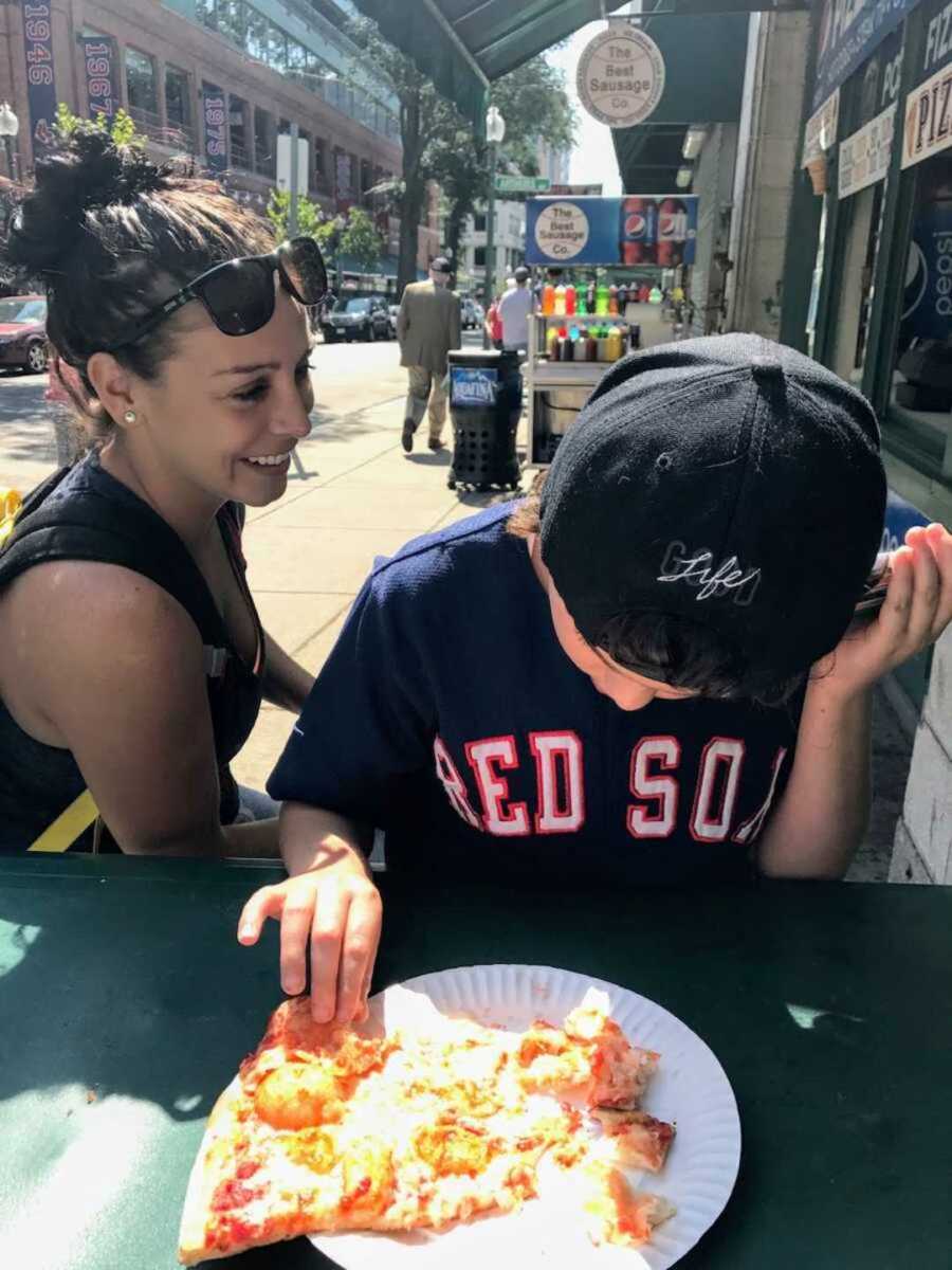 Special needs mom smiling next to son eating pizza