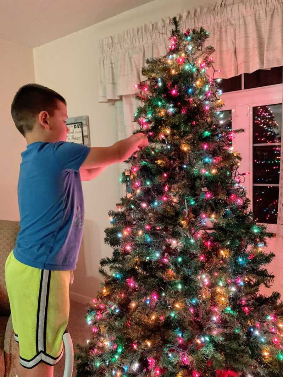 Little boy putting ornaments on the lit up Christmas tree