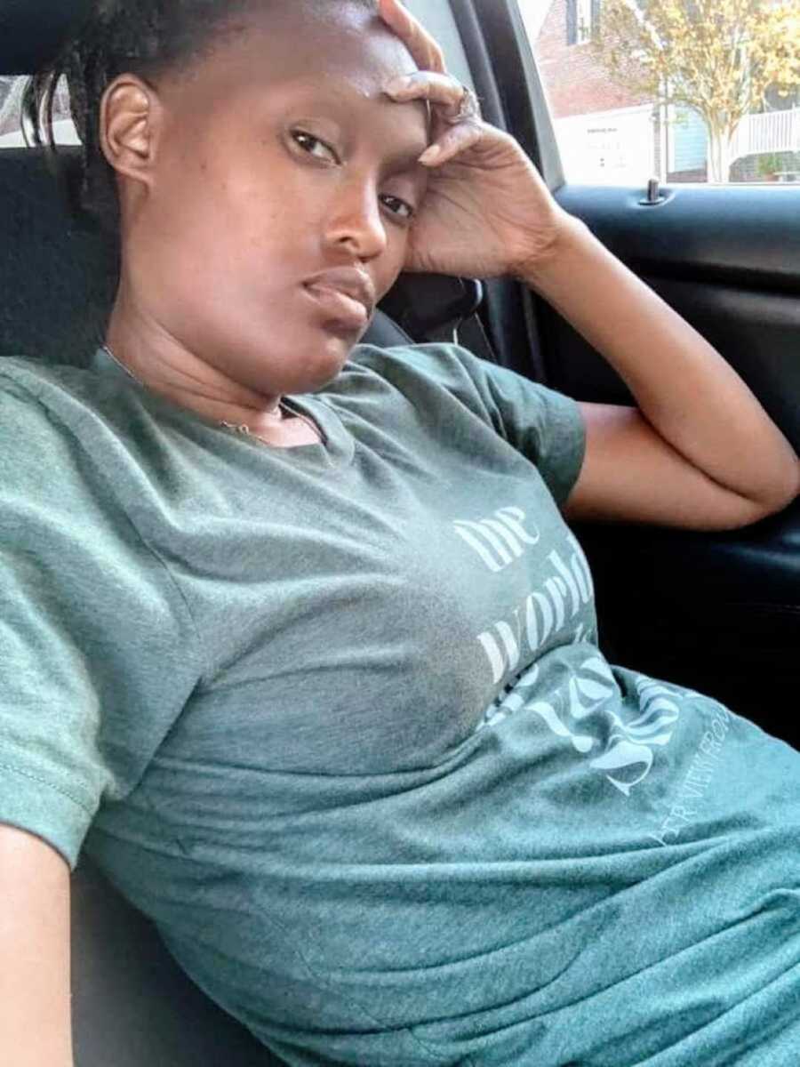 black woman sits in her car and takes a selfie looking defeated
