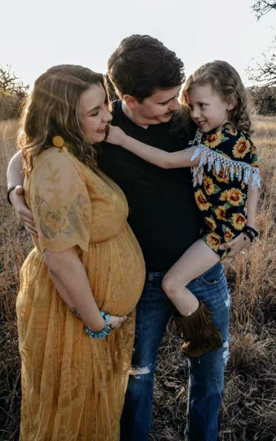 Mom in yellow sundress holding pregnant belly next to family