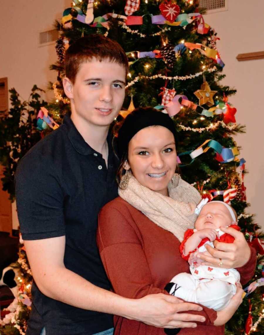 Teen parents holding newborn girl by Christmas tree