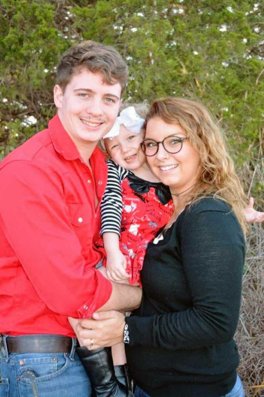 Young couple hugging toddler daughter