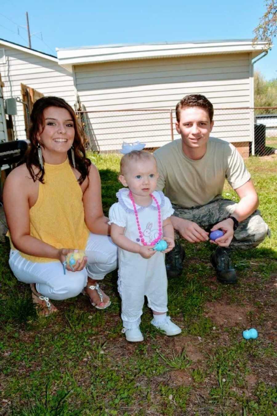 Young parents squatting next to toddler daughter on grass