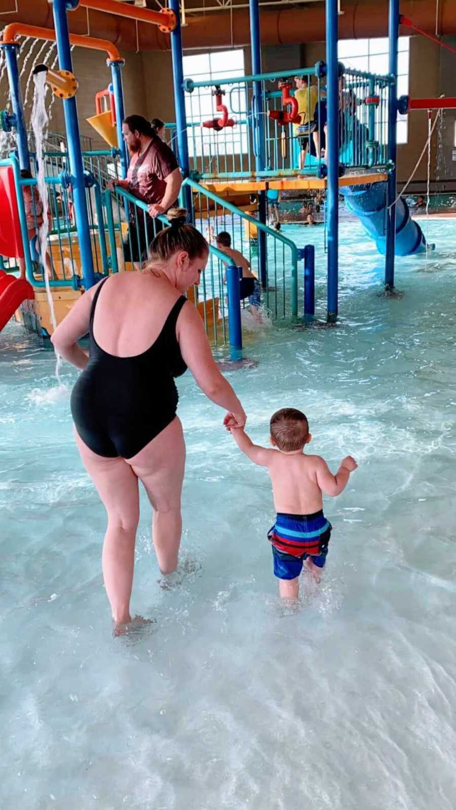 mom wearing one piece bathing suit while holding toddler's hand in waterpark