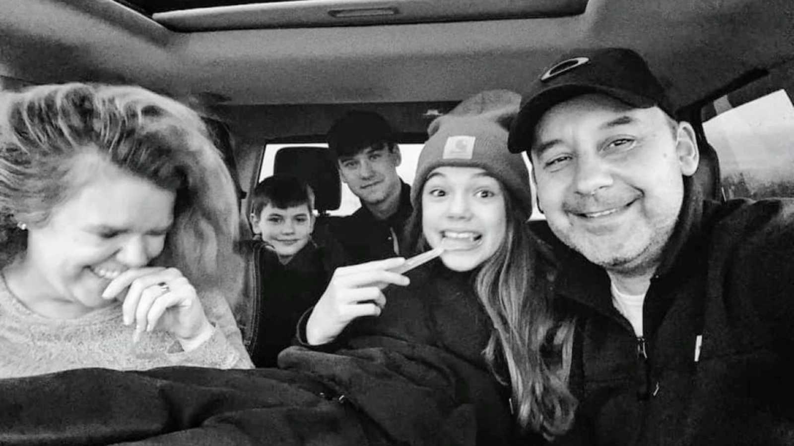 parents take a car selfie with their three teenage children in the backseat