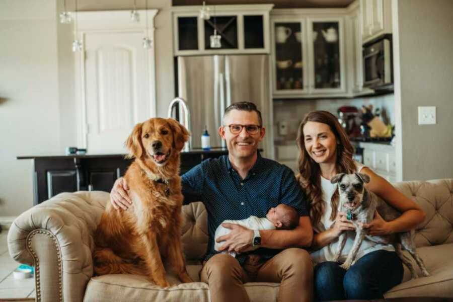 Couple take family photo in their living room with their newborn adopted son and their two dogs