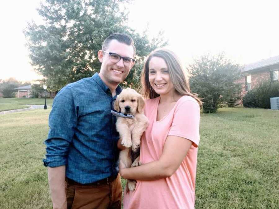 Married couple take photo with their recently adopted golden retriever puppy