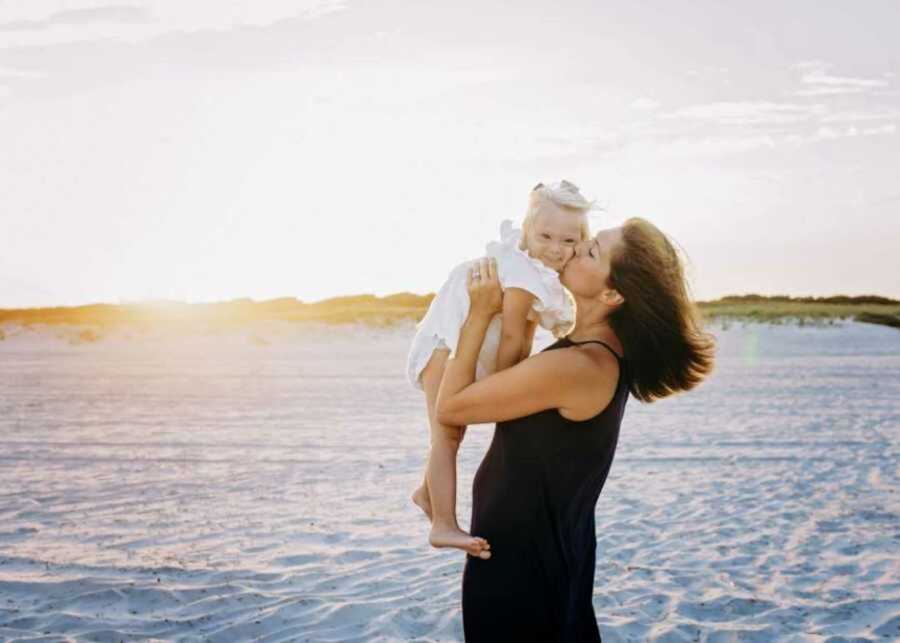 Mom kissing daughter with Down syndrome on beach