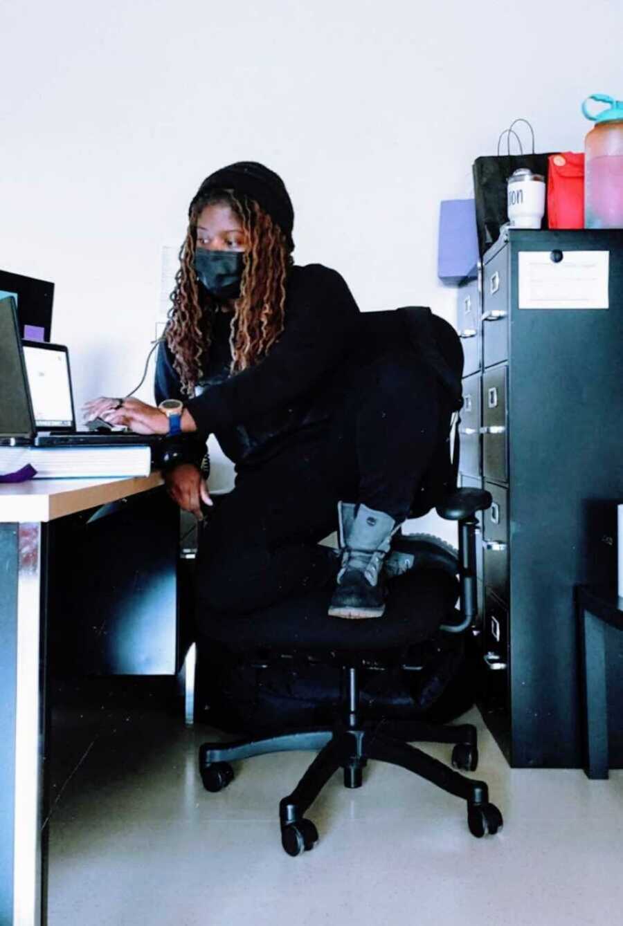 teacher sits at desk wearing face mask