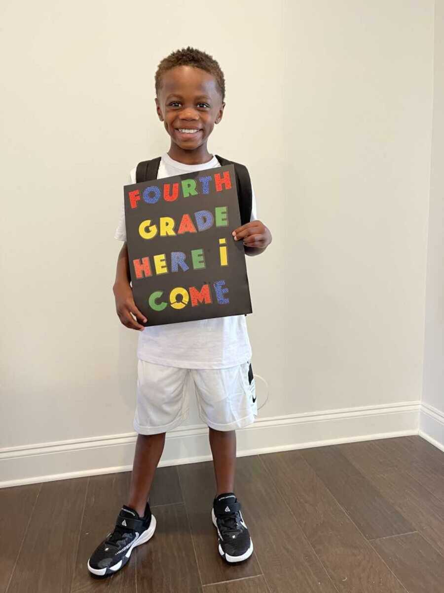 Dwayne wearing a white outfit with a sign ready for fourth grade