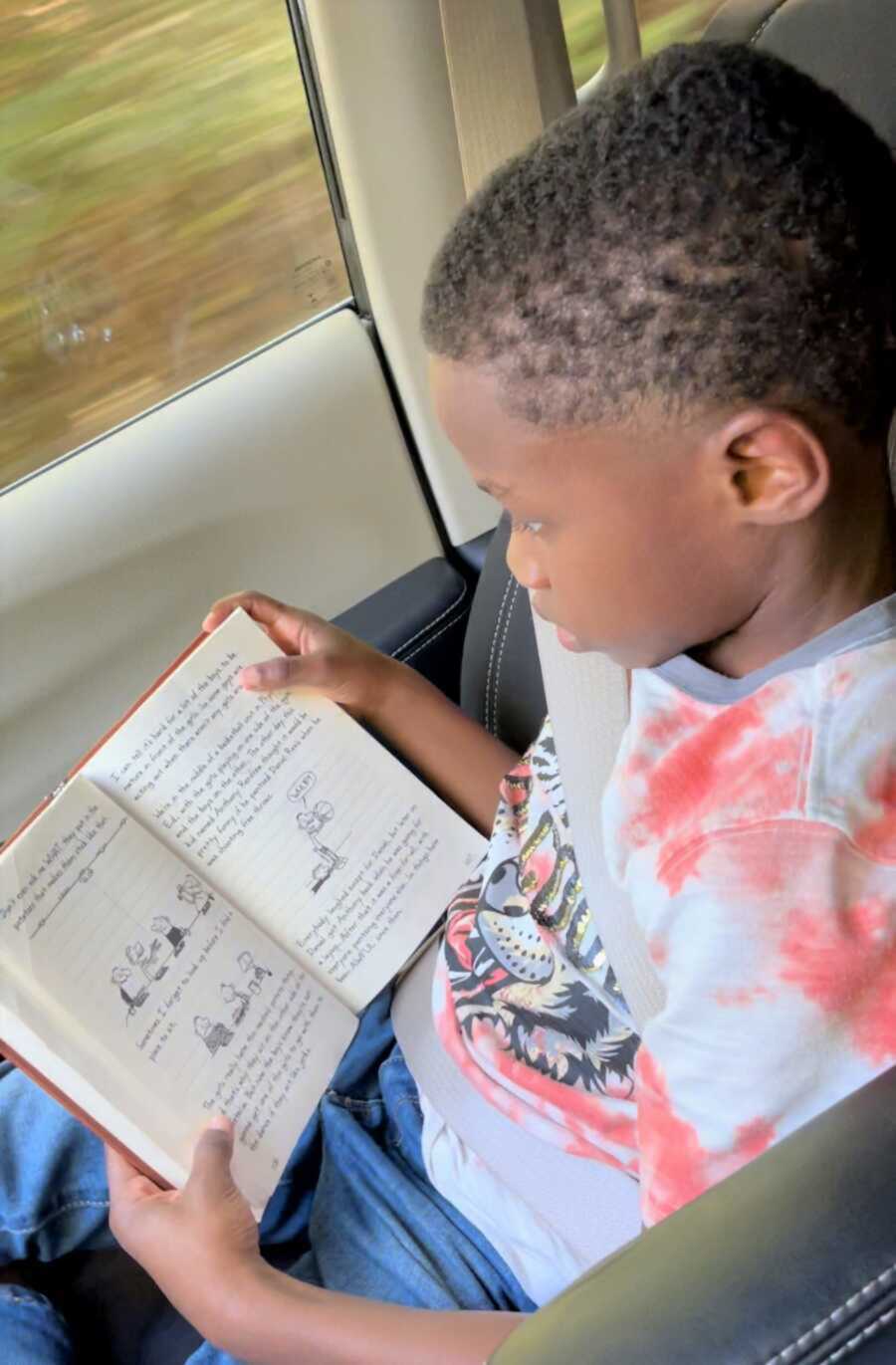 Dwayne is buried in a book as he sits in the car 