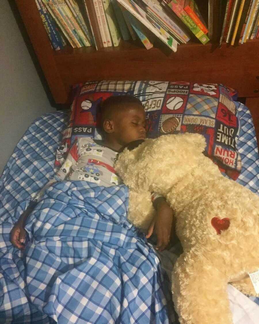 Foster boy sleeps in his blue bed with a stuffed dog 