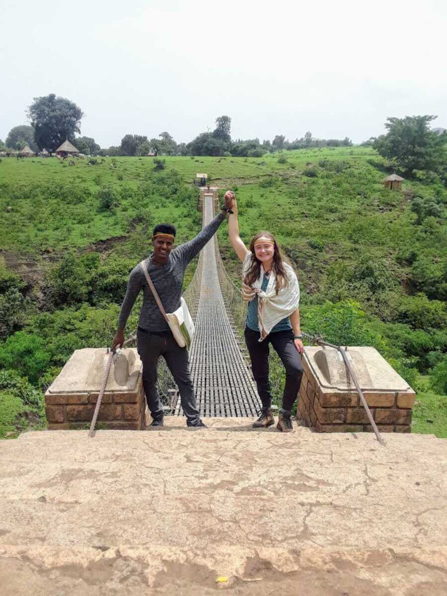 Couple smiling holding up hands together in front of bridge in the forest