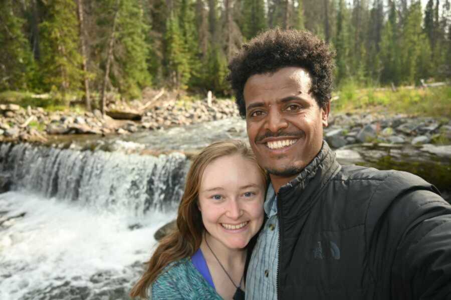 Ethiopian man and American woman smiling in front of waterfall together