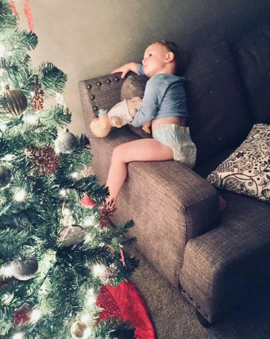 Little boy sitting on arm of couch admiring the lit up Christmas tree