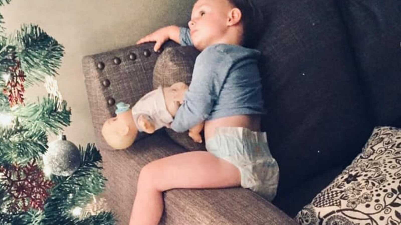Little boy sitting on arm of couch admiring the lit up Christmas tree
