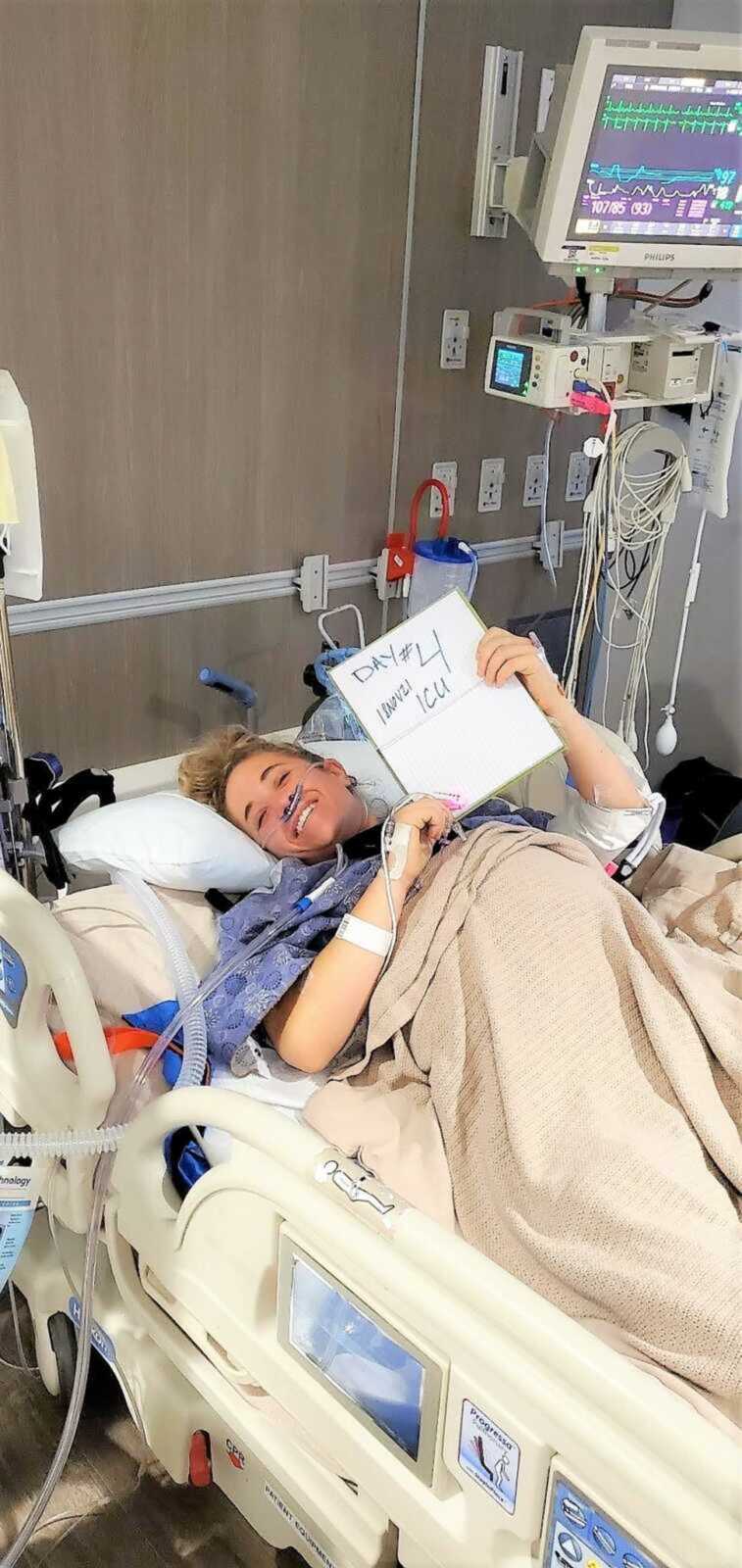 woman laying in a hospital bed with sign that says "DAY 4 ICU"