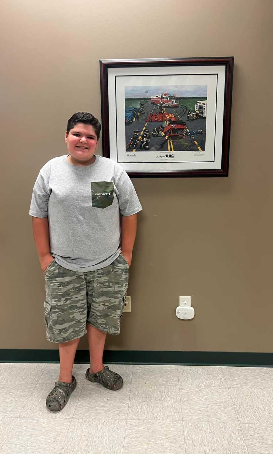 Autistic son standing by framed football photo wearing camouflage shorts and grey shirt