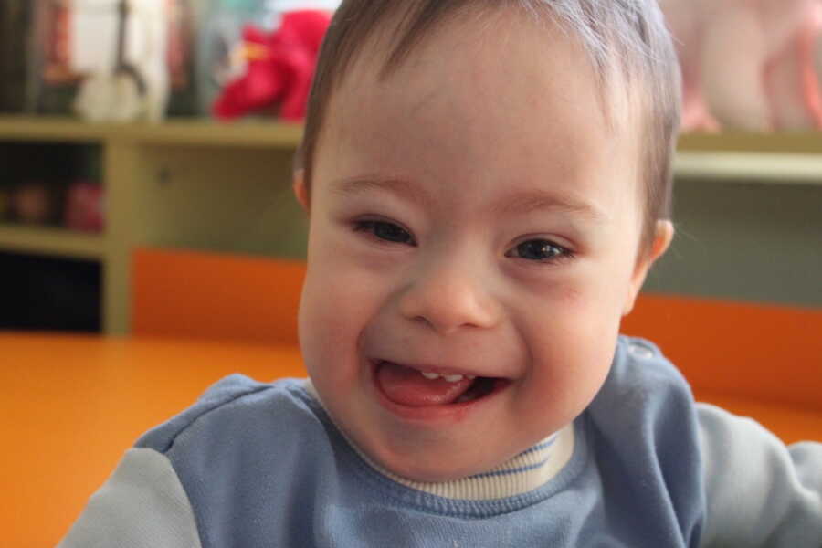 adopted son with Down syndrome smiling in camera wearing blue shirt