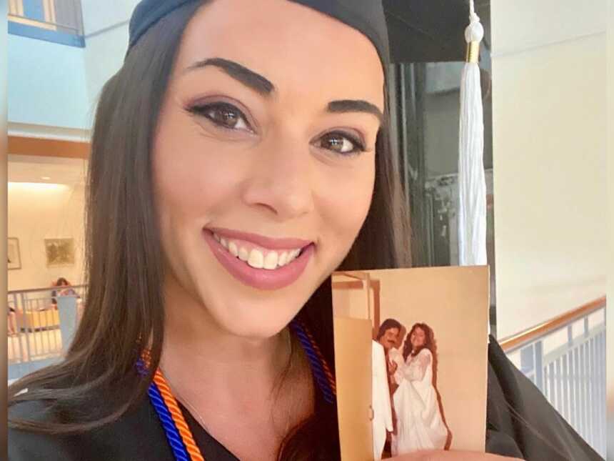 woman holds a photo of her deceased parents while in her cap and gown on graduation day