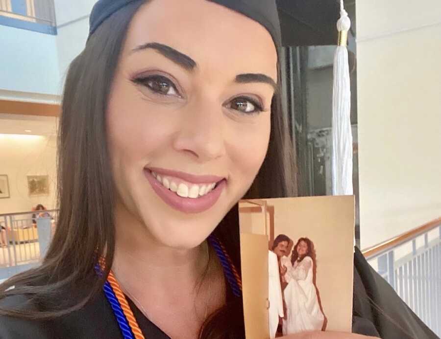 woman holds a photo of her deceased parents while in her cap and gown on graduation day