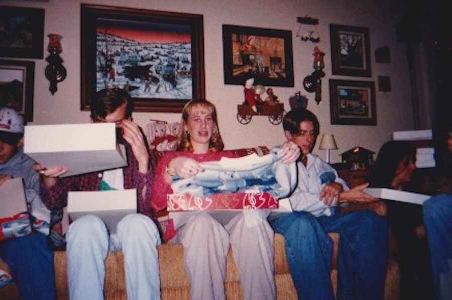 Cousins sitting on yellow couch opening Christmas sweaters sewn by grandma