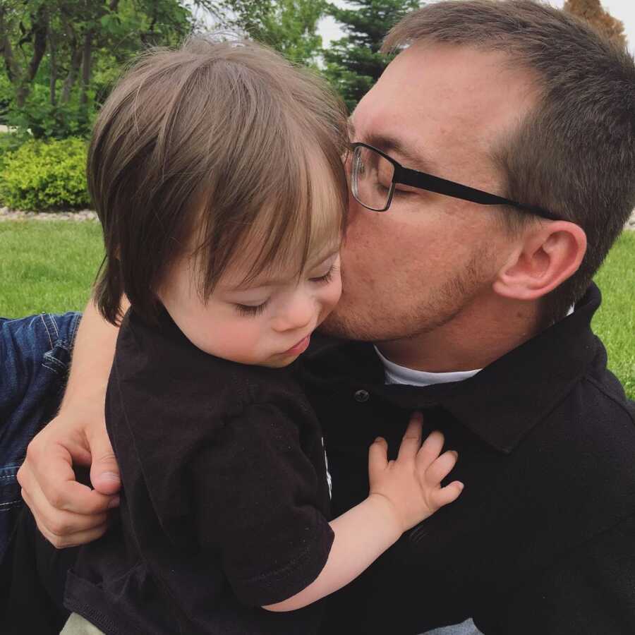 dad kissing his adopted son with Down syndrome on the cheek