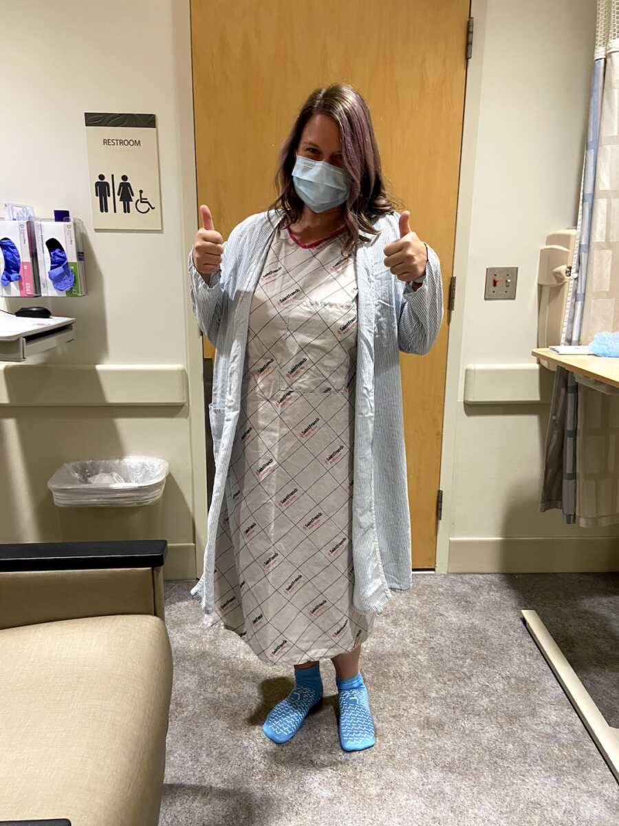 endometriosis warrior stands in hospital gown giving a thumbs up before surgery